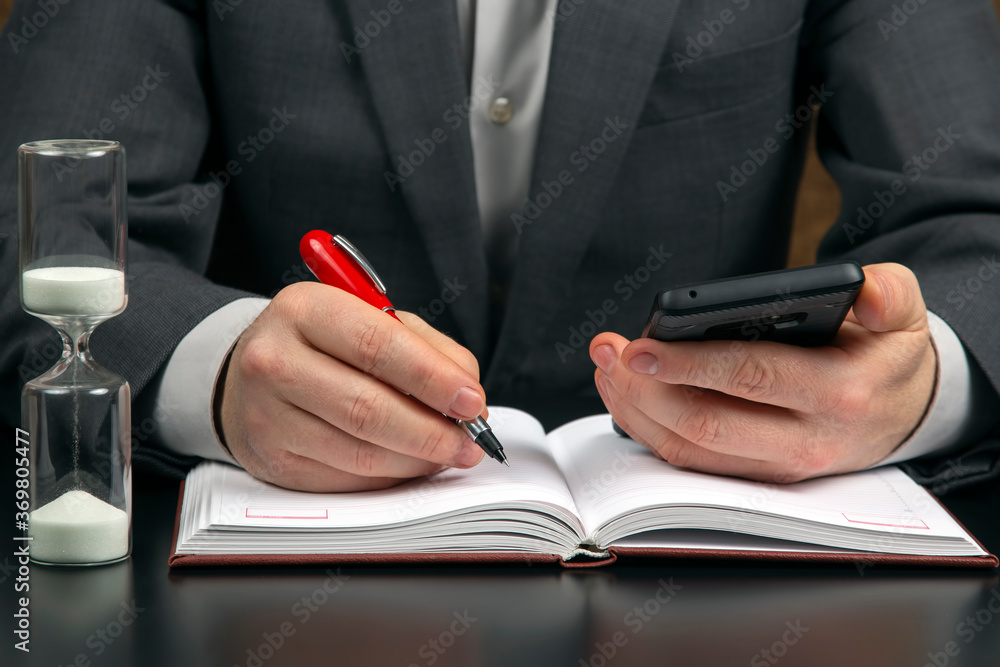 business man in the office is working with a mobile phone on the background of an hourglass. business and successful goal business man in the office is working with a mobile phone on the background of an hourglass. business and successful goal