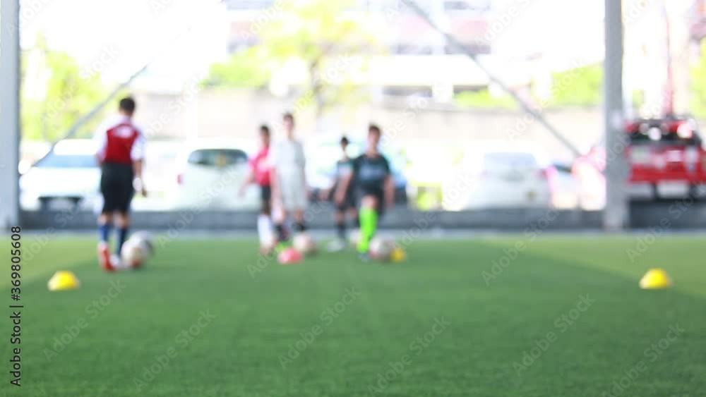 Blurry coach is coaching kid player with ball and soccer training equipment on green artificial turf. Blurry background football training in soccer academy. Sport blurry background.