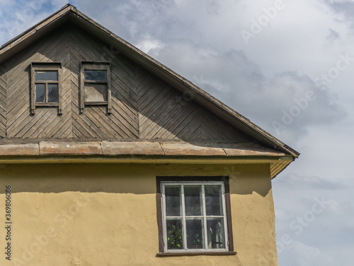 Small rustic yellow house with a wooden roof against the backdrop of a cloudy sky.
