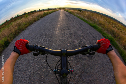 Cyclist in red gloves rides on the road towards sunny sunset sky. Sports and travel.