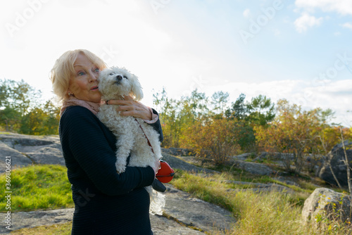 Wallpaper Mural Senior woman looking shocked while holding dog on boulder in the mountains Torontodigital.ca