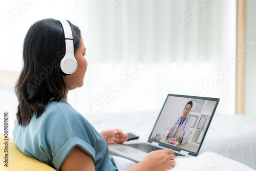 Back view of Asian woman making video call with her doctor with her feeling sick on laptop in bedroom for online healthcare digital technology service consultation while staying at home.