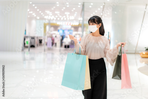 Photography Asian woman wearing mask over her face while walking at shopping mall with shopping bag for healthcare and prevention from coronavirus, Covid19 influenza in crowded place