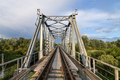 Big metal railway bridge over the river at sunset in summer.