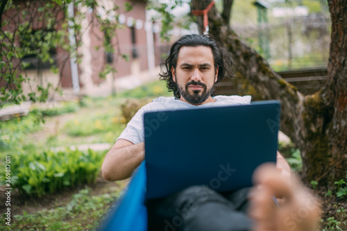 A man works with a laptop in a hammock in a country house