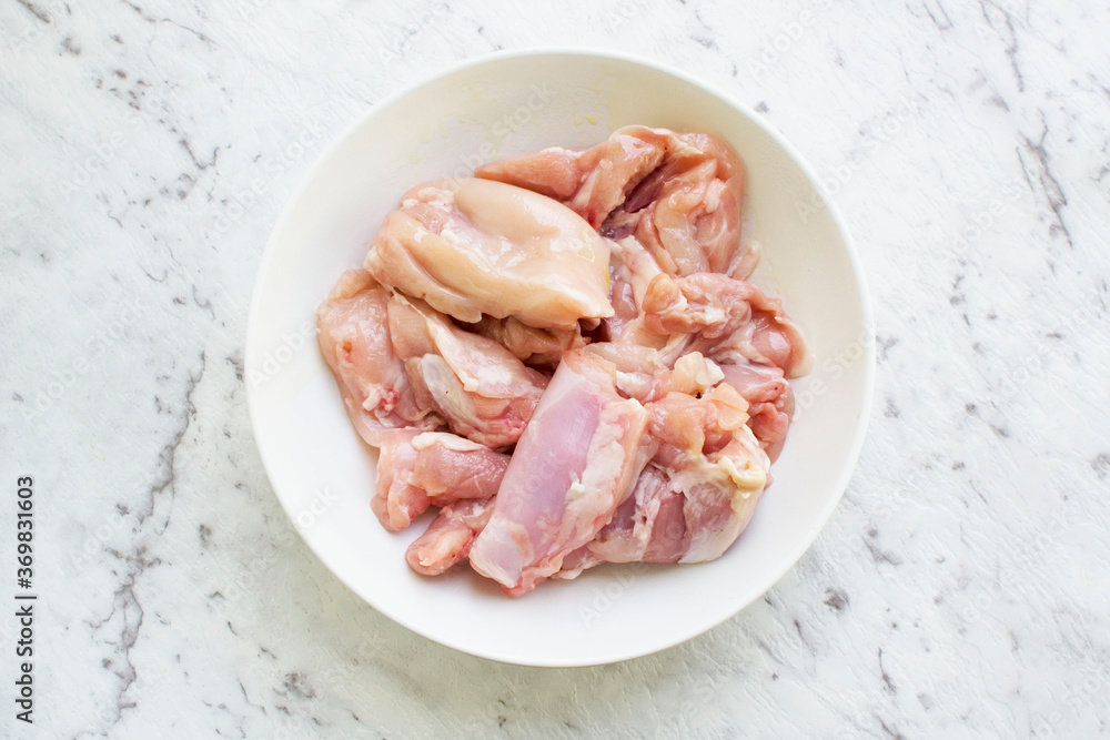 Raw chicken thighs in a bowl on a white marble background Raw chicken thighs in a bowl on a white marble background