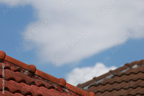 Old red brick roof tiles on blue sky and white cloud background, selective focus