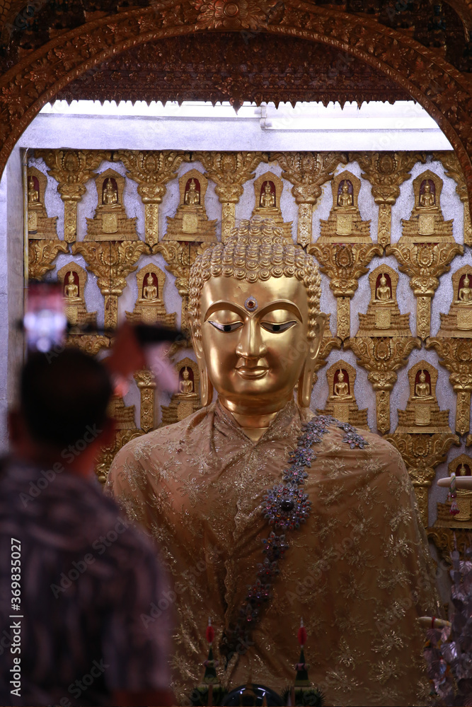 Fototapeta premium Close up face of buddha sculpture in the building of Wat San Pa Yang Luang temple with blurred people or tourism