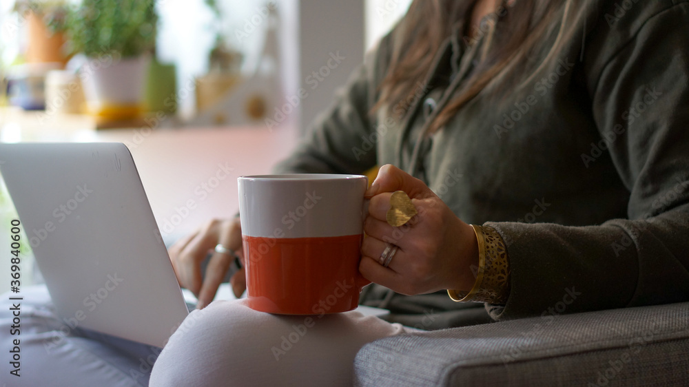 Woman using laptop with a cup of coffee in the other hand working from home Woman using laptop with a cup of coffee in the other hand working from home