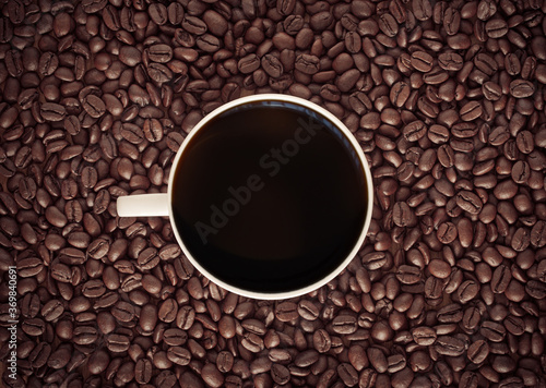 Black coffee cup with roasted coffee beans background.