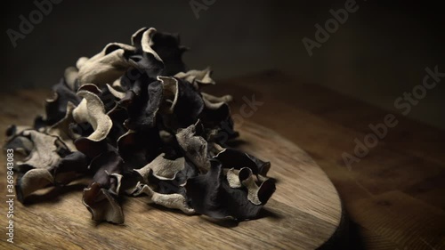 Close up shot of rotating dry black sliced mushroom on wooden background. Edible dark fungus - auricularia polytricha. Nobody