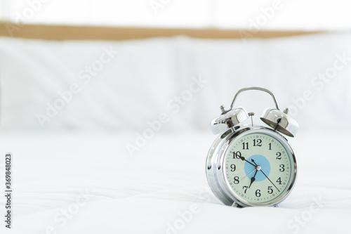 Retro vintage style analog alarm clock on the white bed close up with copyspace. Asleep and exhausted working people in the morning. Retro analog alarm clock almost 7 O'Clock.