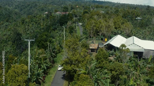 Aerial of a white car driving along the winding mountainous roads of the Bedugul resort area of Bali. Tracking aerial drone photo