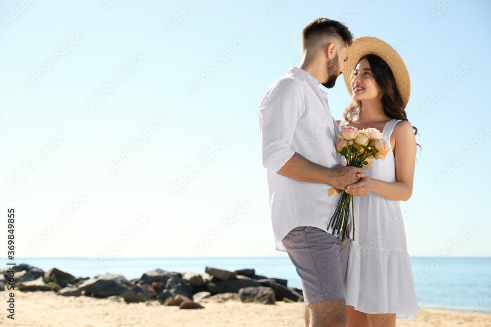 Happy young couple with flowers on beach near sea. Honeymoon trip Happy young couple with flowers on beach near sea. Honeymoon trip