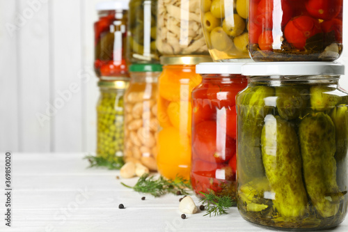Glass jars with different pickled foods on white wooden background, closeup