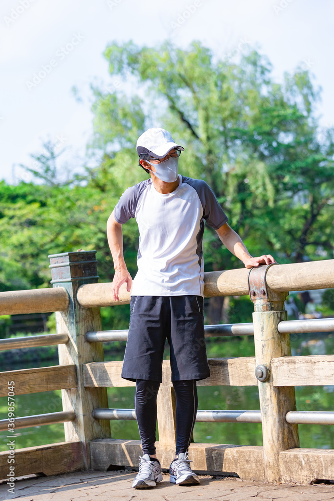 熱中症の恐れのある中年男性が、マスクをつけながら野外で運動をしている 熱中症の恐れのある中年男性が、マスクをつけながら野外で運動をしている