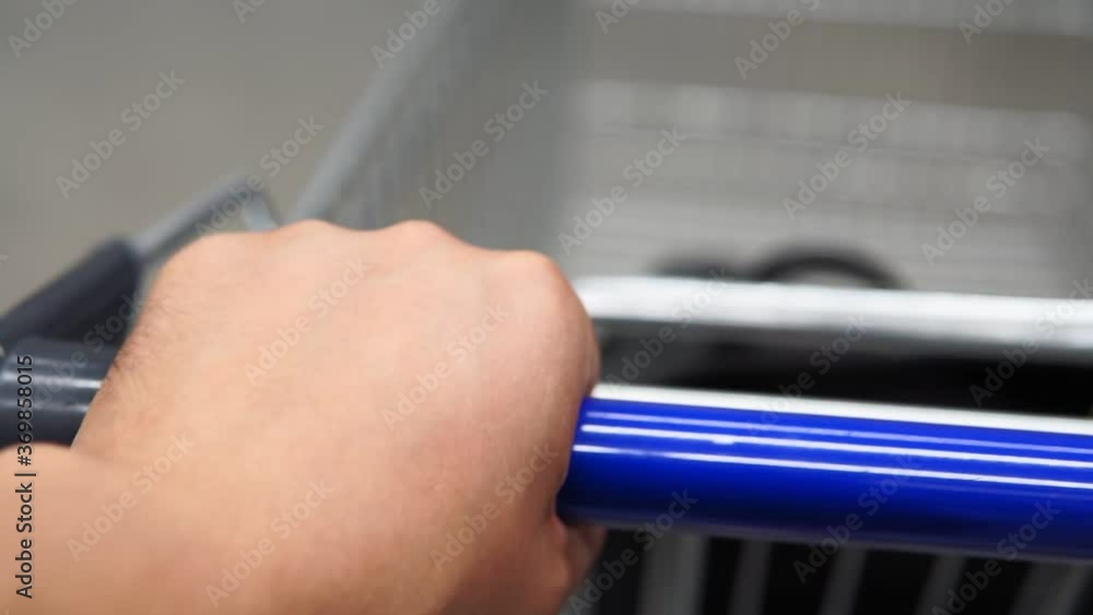 Male left hand holding shopping cart grip handle, pushing pass the shelf in supermarket. First-person view close up. Male left hand holding shopping cart grip handle, pushing pass the shelf in supermarket. First-person view close up.