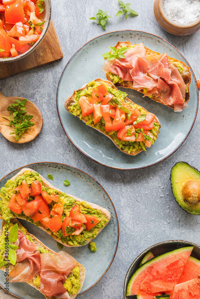 Homemade bread with avocado spread, chopped tomatoes and herbs. Bread with Parma prosciutto ham. Healthy breakfast concept seen from above. With copy space. Homemade bread with avocado spread, chopped tomatoes and herbs. Bread with Parma prosciutto ham. Healthy breakfast concept seen from above. With copy space.