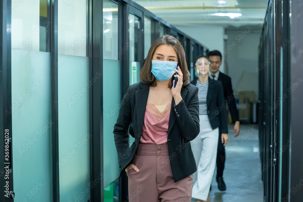 Obraz premium Business workers wearing medical facial mask working as of social distancing policy in the business office during new normal change after coronavirus or post covid-19 outbreak pandemic situation.