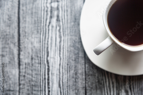 White cup with coffee on a white saucer on a gray wood background