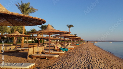 Sandy beach with empty sunbeds. Calm sea. Clear sky.