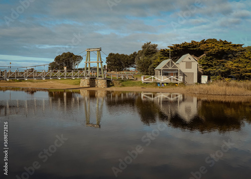 Quiet wooden beachhouse with a suspension bridge and still water in the foreground