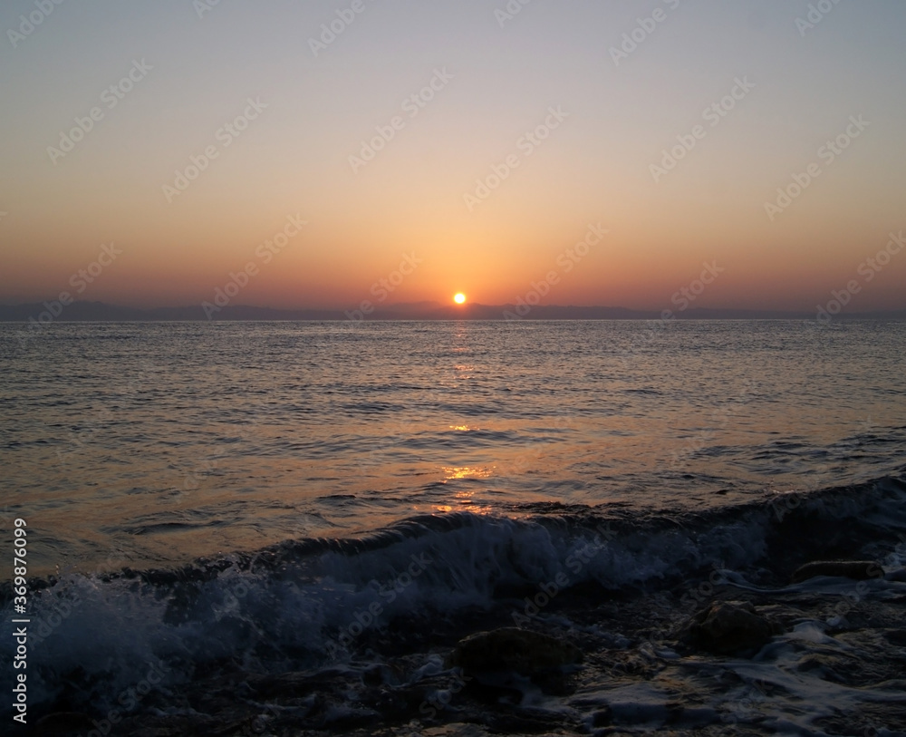 Beautiful dawn over the sea. The sun rises from behind the mountains. Sunny path on the water. Light wave and swell on the surface of the water