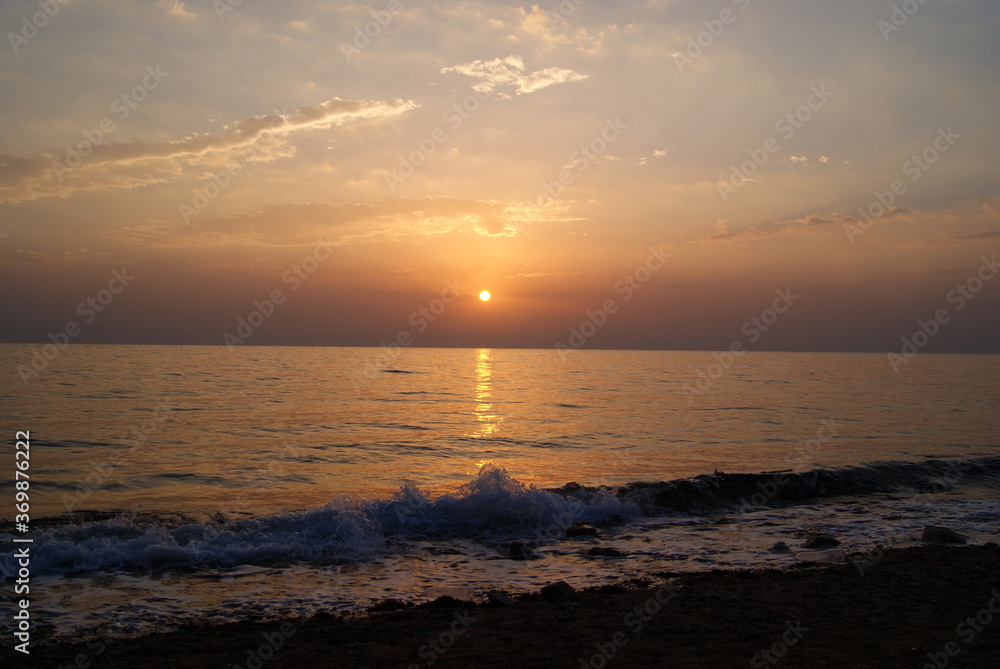 Beautiful dawn over the sea. The sun rises from behind the mountains. Sunny path on the water. Light wave and swell on the surface of the water