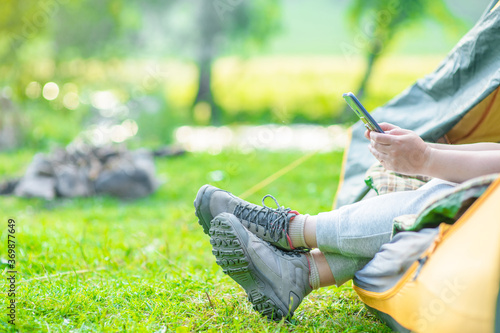 Woman sits inside tend and checks a smartphone for internet contacts or work while sits inside tent. Travel and work concept with an alternative and adventurer lifestyle