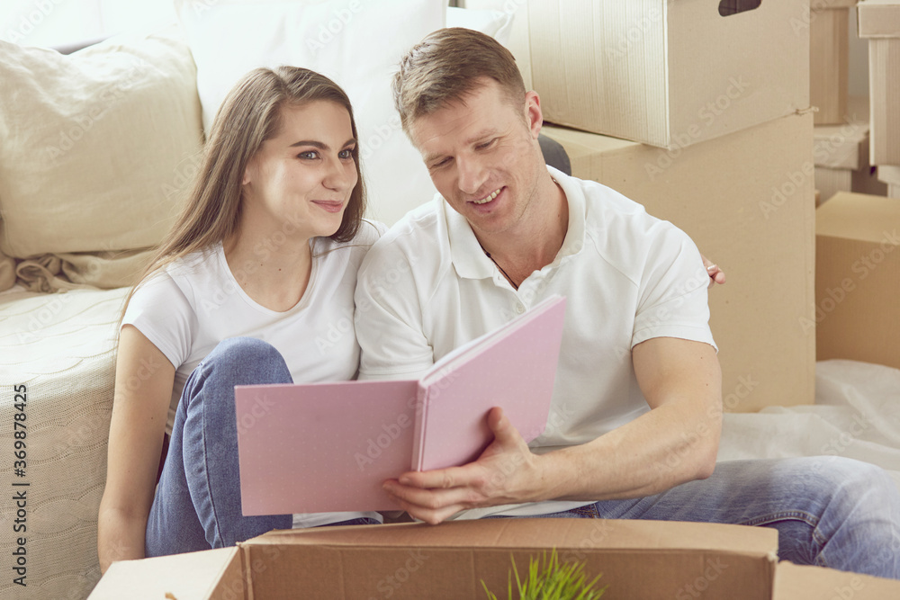 Portrait of happy couple looking at laptop computer together sitting in new house, surrounded with boxes Portrait of happy couple looking at laptop computer together sitting in new house, surrounded with boxes