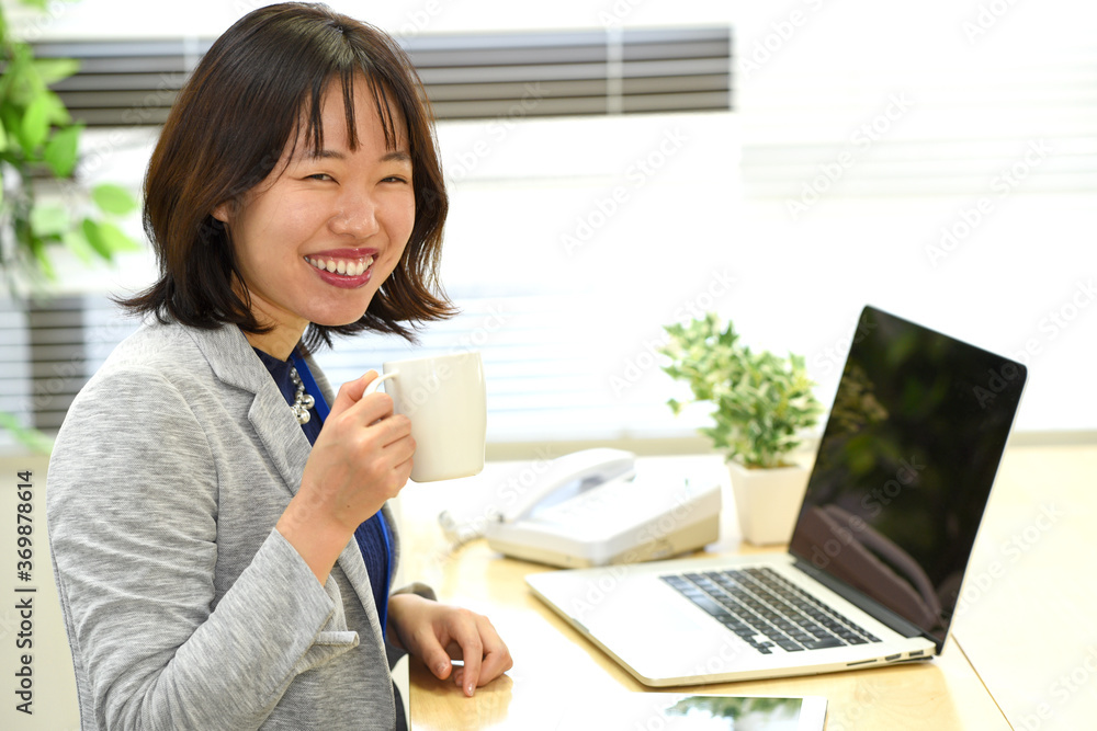 飲み物を飲みながらノートパソコンを操作する若い女性 飲み物を飲みながらノートパソコンを操作する若い女性