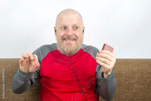 bearded man listens with pleasure at home to his favorite music from the phone with small headphones. audiophile and music lover. music and hi-fi sound.