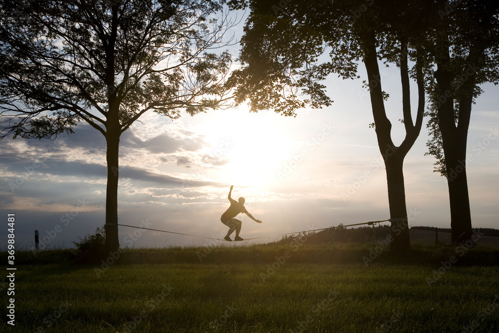 junger Mann balanciert auf der Slackline im Sonnenuntergang