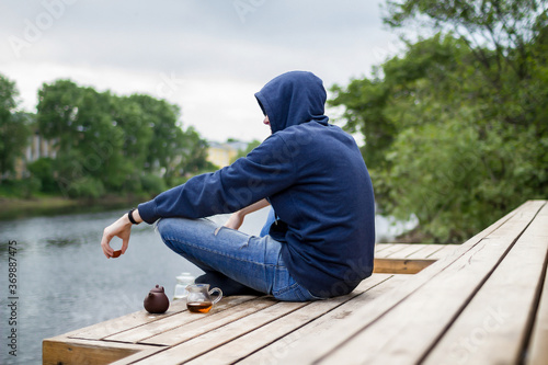 Man in blue hoody drinking tea near river