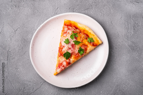 Hot pizza slice with mozzarella cheese, ham, tomato and parsley on plate, stone concrete background, top view