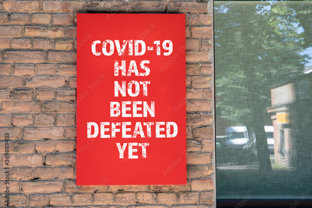 Obraz premium COVID-19 HAS NOT BEEN DEFEATED YET. Red advertising sign on the masonry wall