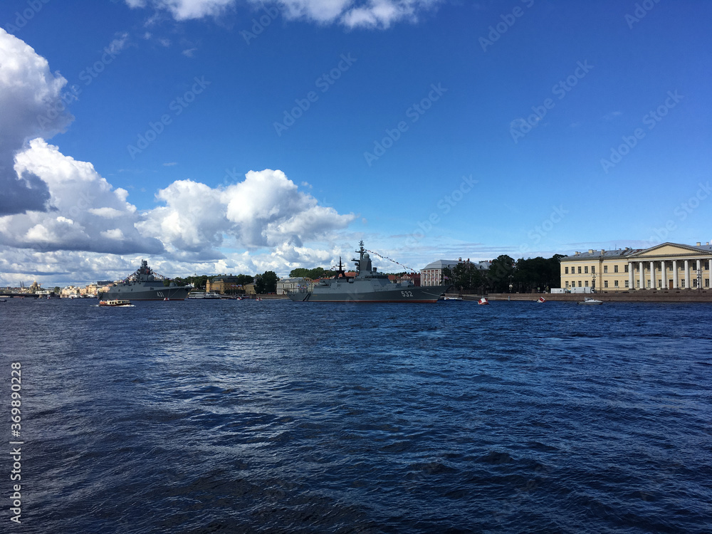 Warships in the water area of ​​the Neva, arrived to participate in the naval parade held in St. Petersburg against the backdrop of sights and blue sky with clouds.