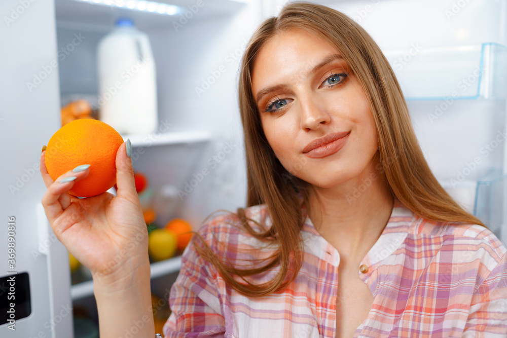 Portrait of a young blonde woman taking food from her fridge