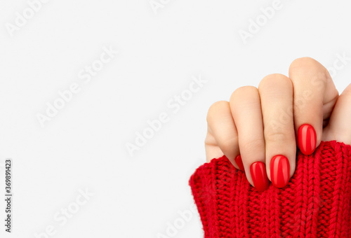 Woman's hand in sweater with red manicure on gray background