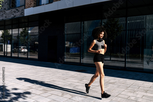Healthy and athletic African woman running on the city street. A biracial girl is jogging in the morning. Full length