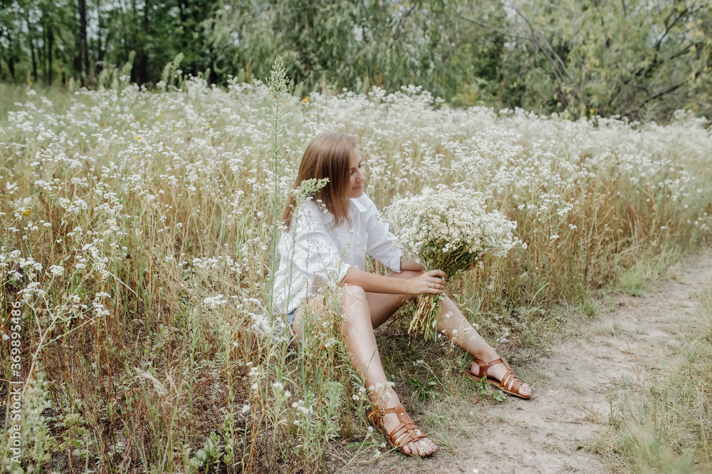 Romantic woman sitting on the footpath in a summer forest. She sits with bouquet of wild flowers in her hands Romantic woman sitting on the footpath in a summer forest. She sits with bouquet of wild flowers in her hands