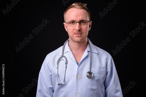 Handsome man doctor with blonde hair against black background