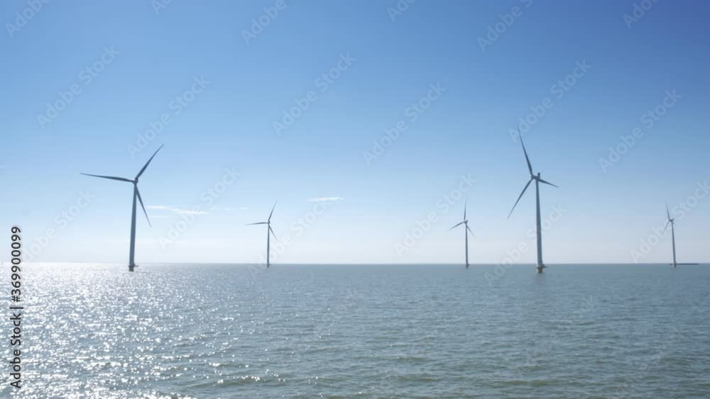 Row of wind turbines in a windpark next to a levee in the IJsselmeer in Flevoland, The Netherlands, with a blue sky above. Row of wind turbines in a windpark next to a levee in the IJsselmeer in Flevoland, The Netherlands, with a blue sky above.