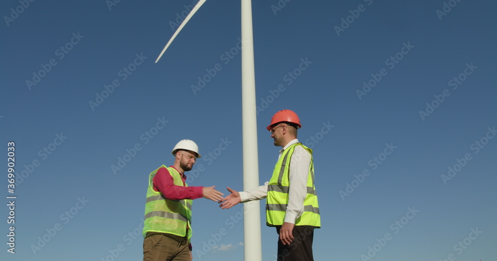 Engineers shake hands. In the background - an air windmill Engineers shake hands. In the background - an air windmill