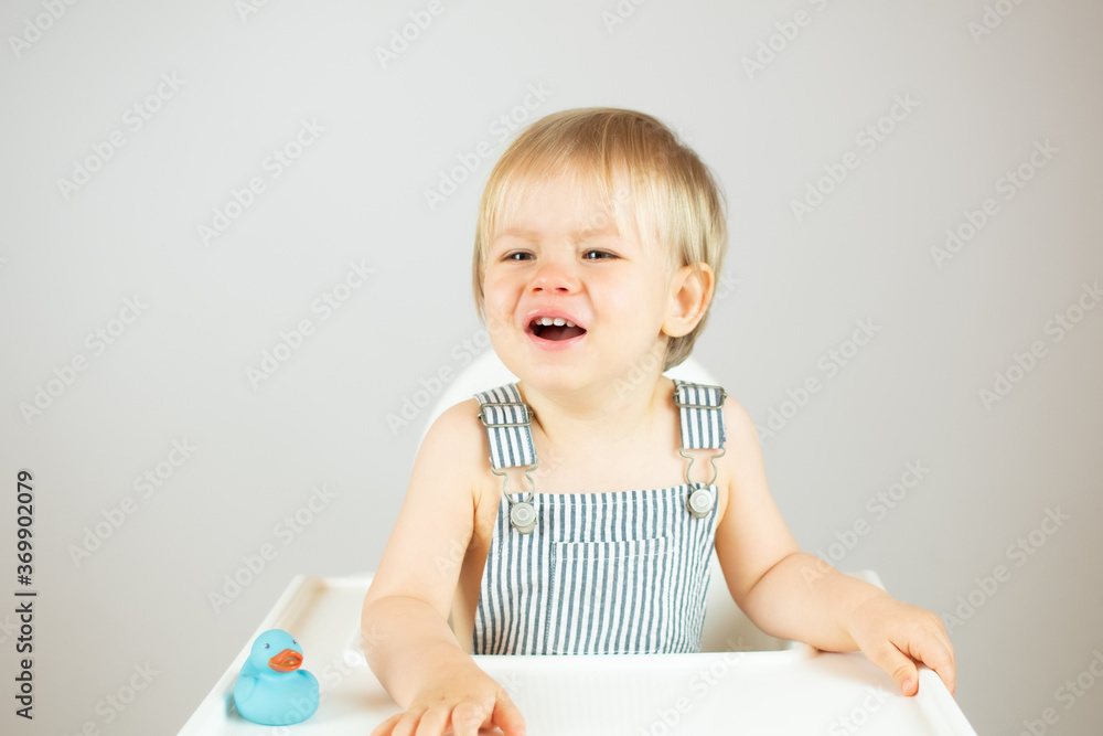 Blond baby with striped overalls sitting and angry
