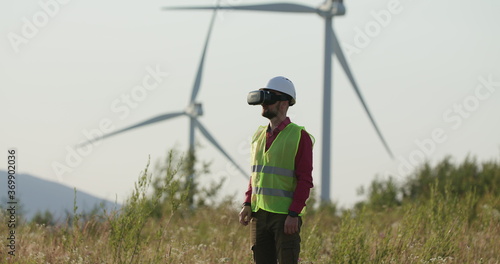 Engineer in VR glasses looking at graphs, turning pages. Windmills in the background