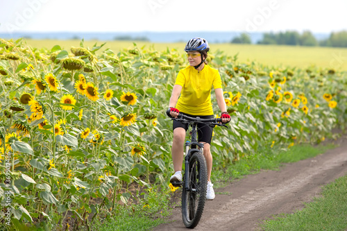 Beautiful girl cyclist rides a field with sunflowers on a bicycle. Healthy lifestyle and sport. Leisure and hobbies