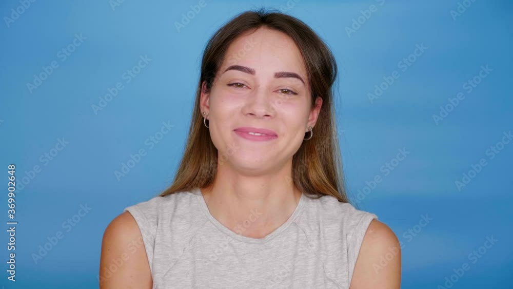Beautiful cheerful woman in gray t-shirt laughs on blue background with copy space. 4K slow motion footage Beautiful cheerful woman in gray t-shirt laughs on blue background with copy space. 4K slow motion footage