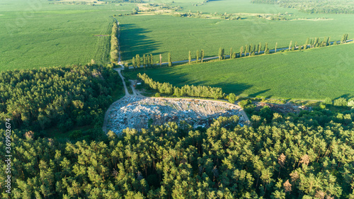 Aerial drone view large city garbage dump near green forest, fields, road at summer sunset. Ecological disaster environment, pollution planet, plastic