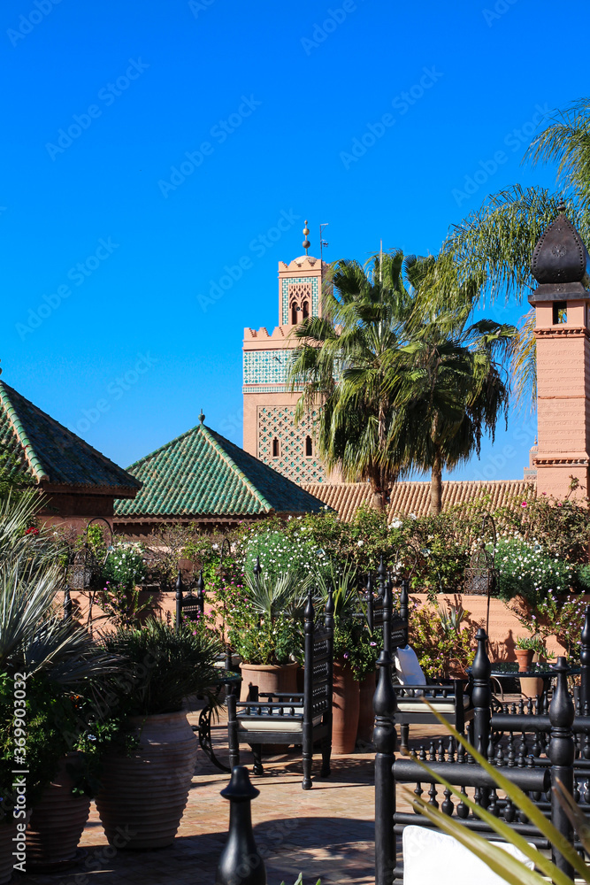 Moroccan Riad with flowers, palm trees, original lamp and view of the mosque of al-Koutoubia. Marrakech, Morocco